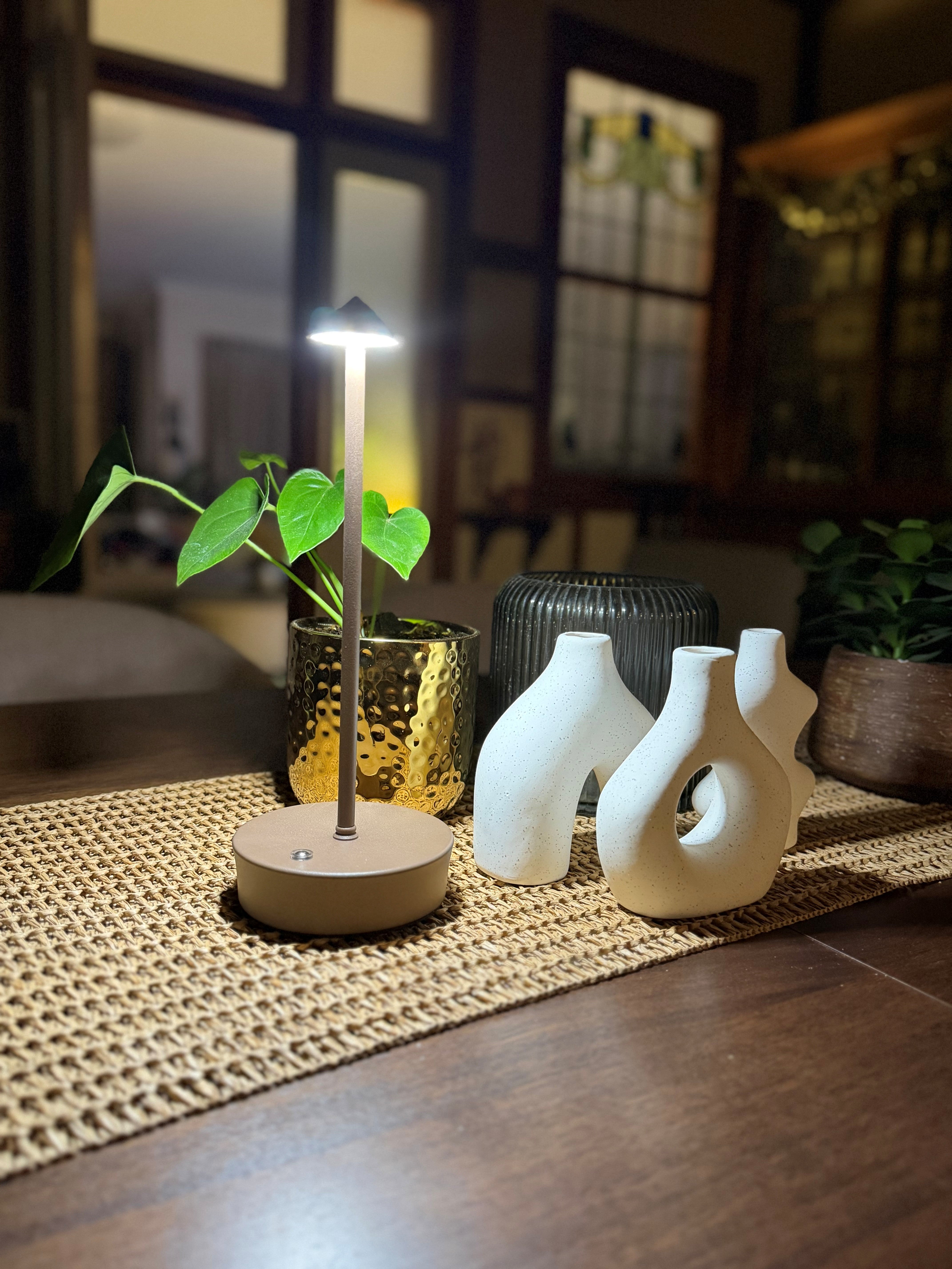 brown halo light table lamp on a woven mat with decorative vases and plants in a blurred indoor setting